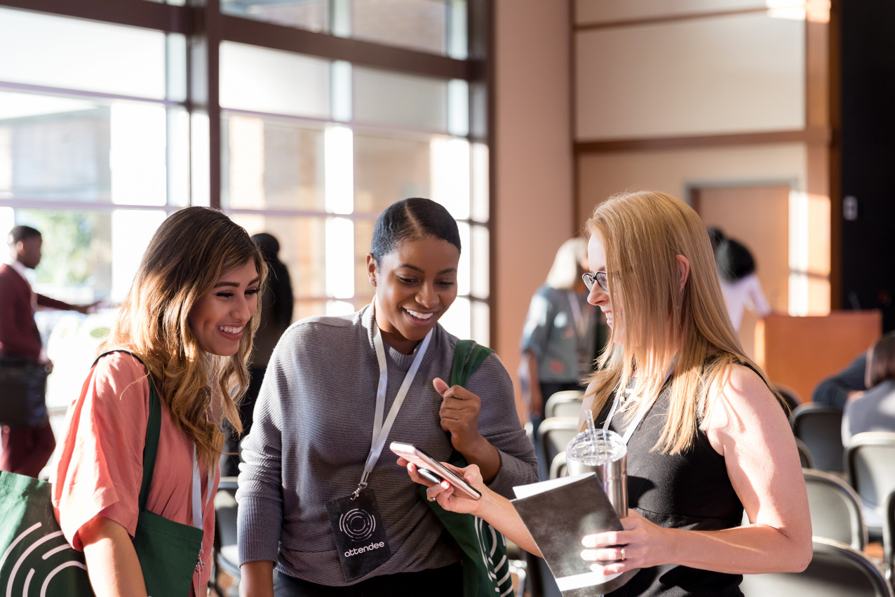 Diverse women attending expo smile at smart phone photos